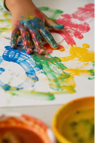 Child's hands covered in bright paint while finger painting on paper
