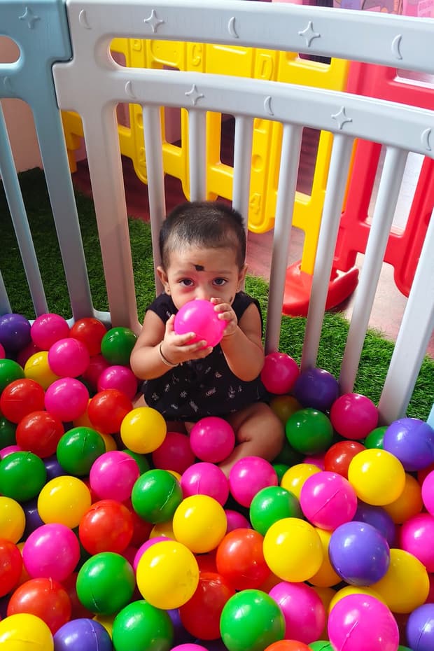 Toddler sitting happily among colorful play balls in the soft play area at Tiny Cradle